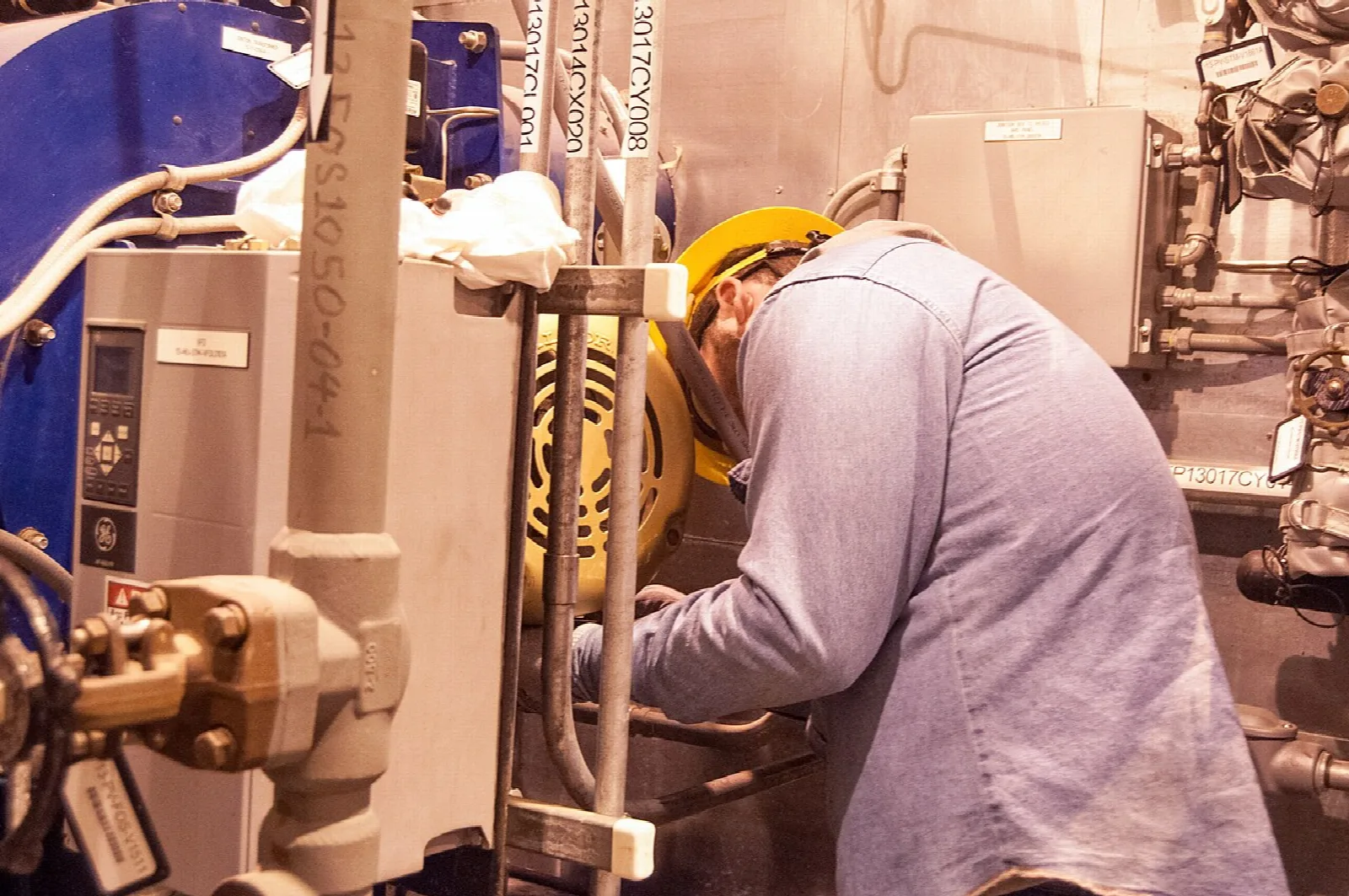 Profissional em atividade de manutenção junto a equipamento industrial.